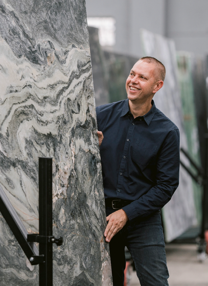 Nathan in the warehouse beside a slab of swirling grey stone